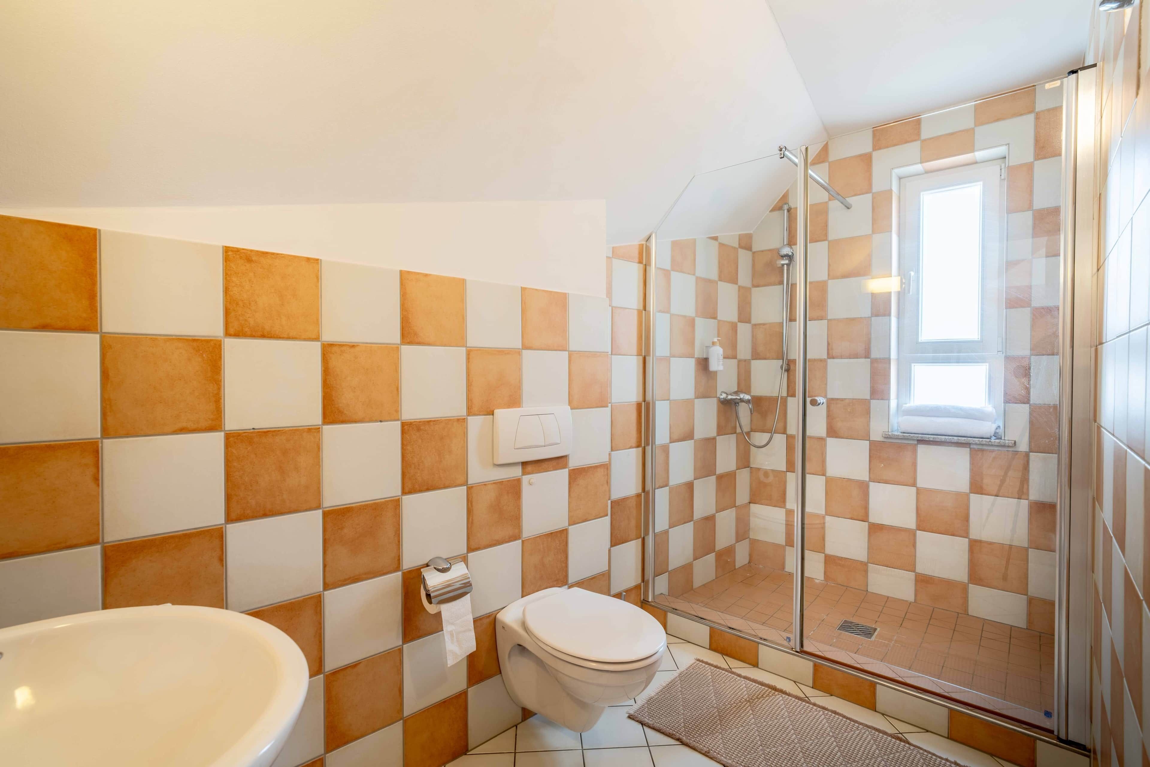 A bathroom with a checkered tile wall, a toilet, a shower, and a sink.