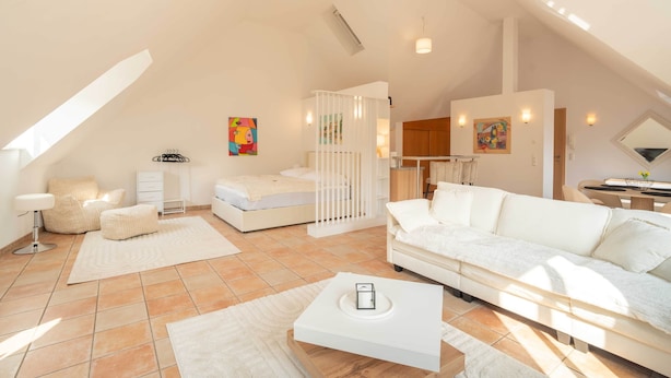 A modern, well-lit living room with a white sofa, a small white table, and a bed with a white headboard. - Stylish Apartment | WiFi, Sky TV & Nespresso (Sobernheim)