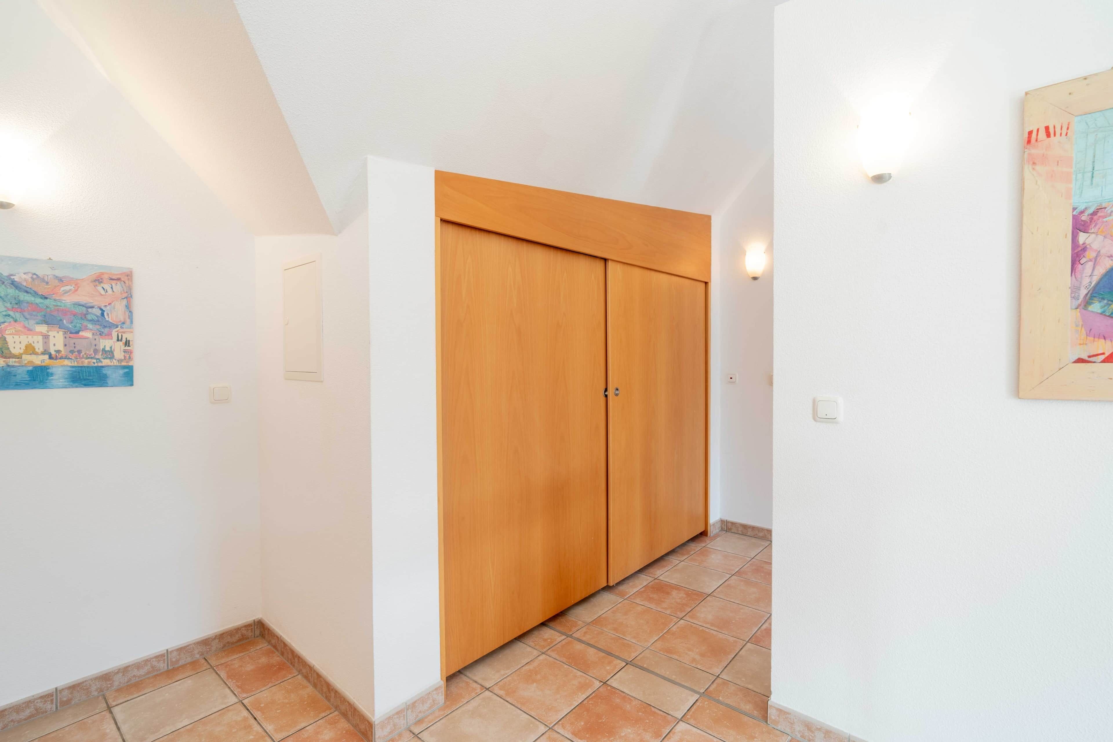 A hallway with a wooden wardrobe, a tiled floor, and a painting on the wall.