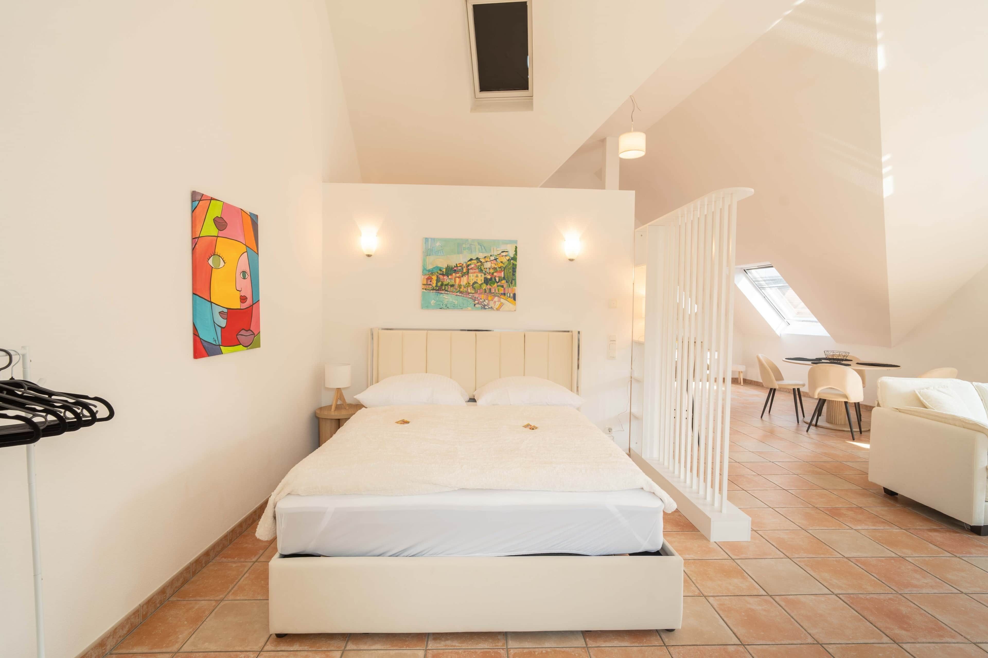 Ein Schlafzimmer mit einem Bett, zwei Gemälden, einem Nachttisch, einem Schreibtisch und einem Stuhl.