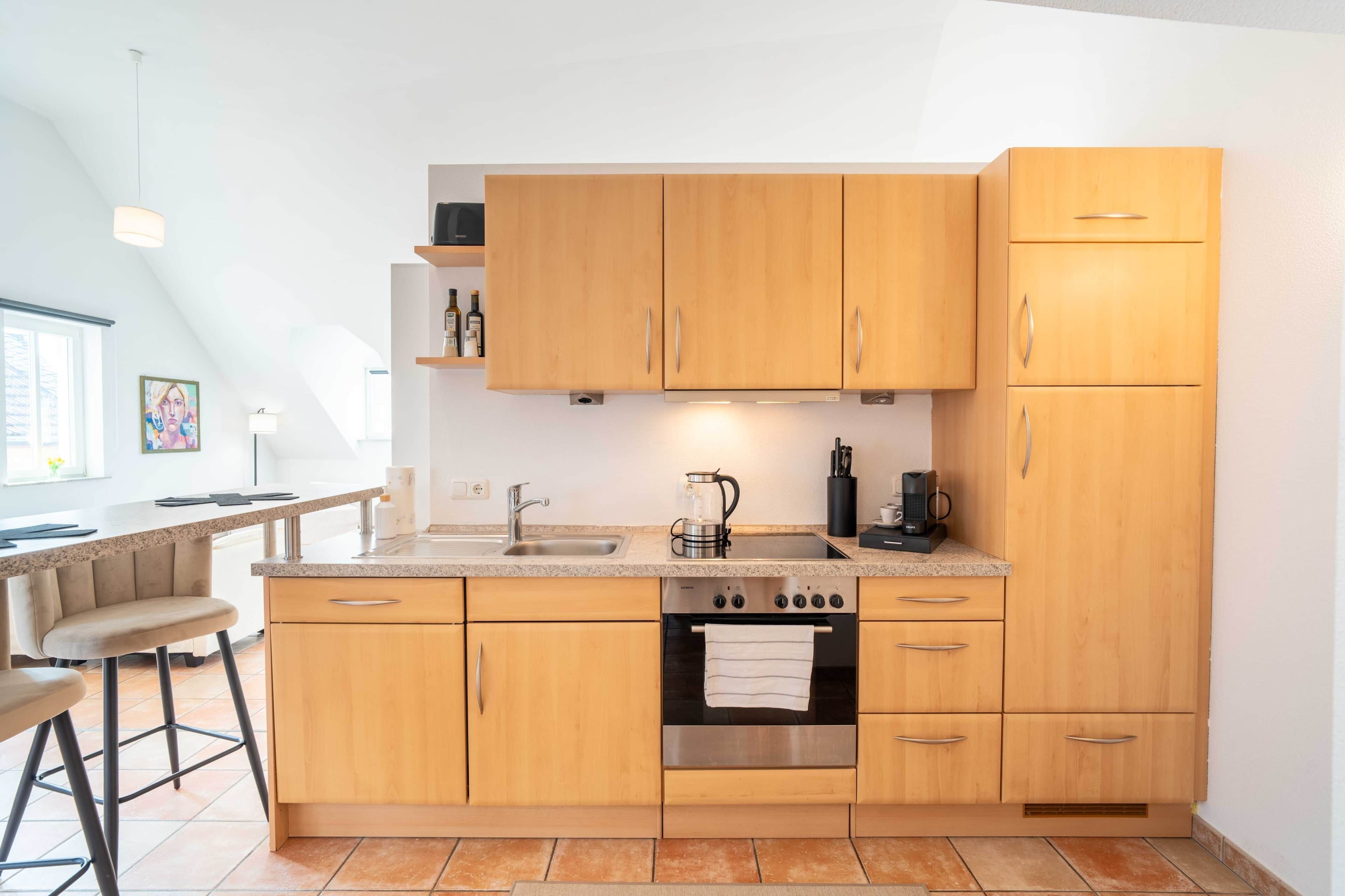 A modern kitchen with wooden cabinets, a stainless steel oven, a coffee maker, and a bar stool.