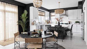 Una cocina moderna con armarios blancos, una isla central y un comedor con una mesa redonda y sillas.