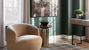 Una habitación con un amplio ventanal, un sillón color beige, un cuadro de un pájaro y una mesa con una planta.