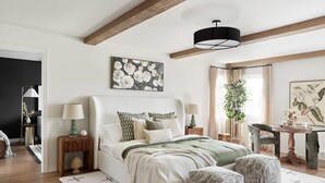 Un dormitorio con cama, mesitas de noche, lámpara, silla, escritorio y una planta colgante.