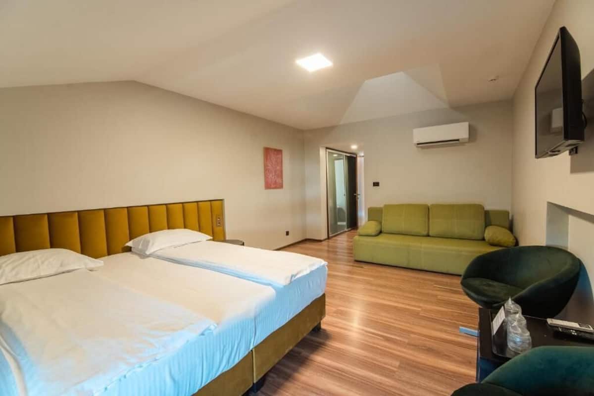 Habitación de hotel con dos camas, un sofá verde, una silla negra y un televisor de pantalla plana.