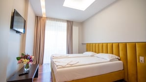 A hotel room with a bed, a TV, a desk, and a window with curtains. - Hotel Vital (Băile Felix)