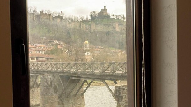 Vista desde una ventana: un puente sobre un río, con edificios y una torre al fondo.