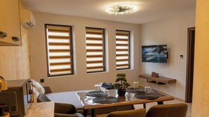Comedor con una mesa dispuesta para cuatro, un televisor montado en la pared y una pequeña planta en maceta en el alféizar.