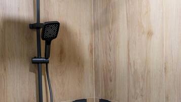 A shower with a handheld showerhead, a wall-mounted control panel, and a corner sink with a black soap dish.