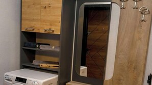 Una habitación pequeña con lavadora, armarios de madera, un espejo y un estante de madera.