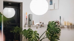A round dining table with chairs, a hanging light fixture, a window with a plant, and a shelf with various items. - Cozy, quiet and family friendly 2-bedroom apartment in Chinatown, NYC (New York)