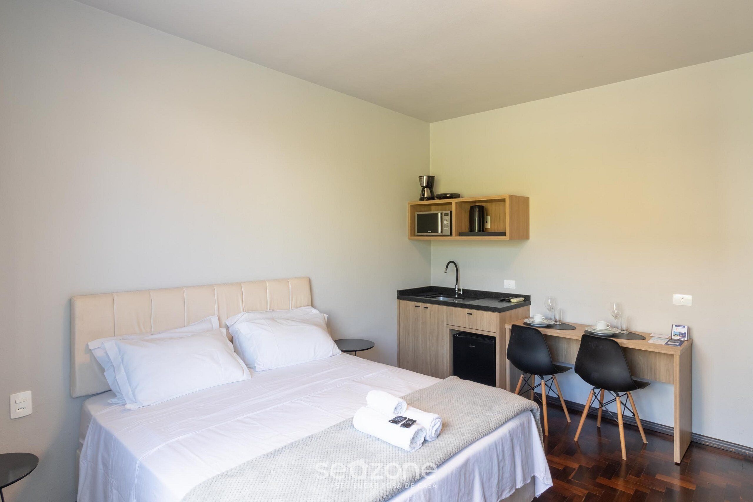 Una camera d'albergo con un letto, una scrivania con due sedie, un angolo cottura e un comodino.