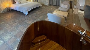 Un dormitori modern amb un llit gran, una zona d'estar amb una cadira i una taula, i una banyera.