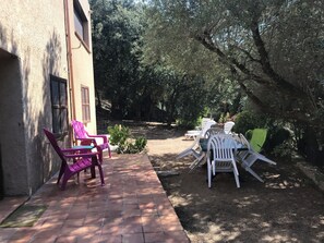 An outdoor patio with chairs and a table, surrounded by trees and a building. - Farniente under the olive trees (Santa-Reparata-di-Balagna)