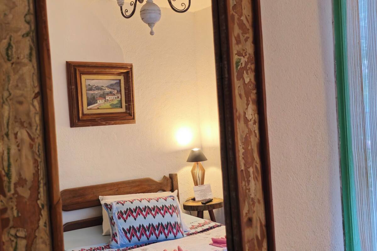 Quarto com cama, mesa de cabeceira, abajur, quadro e espelho.