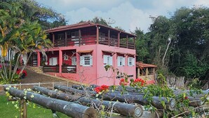 A pink house with a wooden deck, surrounded by greenery and a clear sky. - Pouso Canto de Minas (Tiradentes)