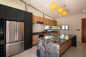A modern kitchen with a stainless steel refrigerator, wooden cabinets, a marble island, and pendant lighting. - Brand New 3BR Pool Home in Uvita Near Marino Ballena with Pool (Uvita)