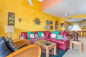 Ein Wohnzimmer mit rotem Sofa, Korbstühlen, einem Glastisch und einem Essbereich mit Tisch und Stühlen.