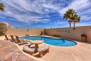 Ein Pool mit Liegestühlen und einem Tisch, umgeben von einer niedrigen Mauer und Palmen.
