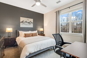 A bedroom with a bed, two bedside tables with lamps, a chair, a desk, a window with a view, and a ceiling fan. - Cozy 2-bedroom apartment in marvelous Asheville with gym access (Asheville)