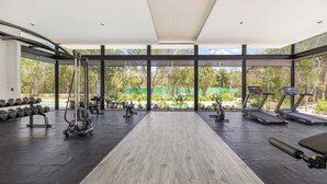 A gym with treadmills, dumbbells, and weight machines, large windows, and a view of greenery. - Family House w Private Pool Rooftop & BeachClub (Solidaridad)