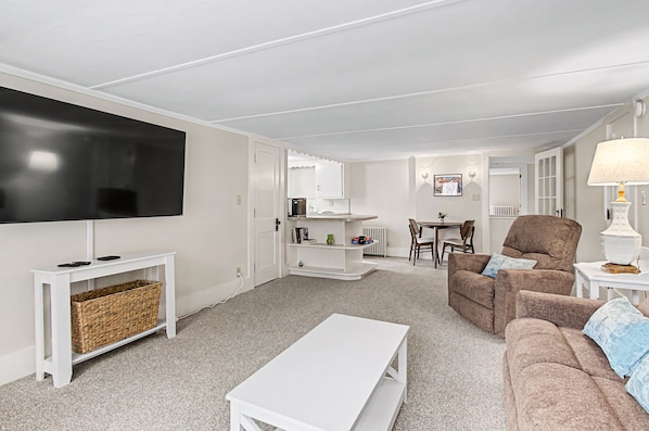 A living room with a TV, white furniture, a sofa, a coffee table, and a lamp.