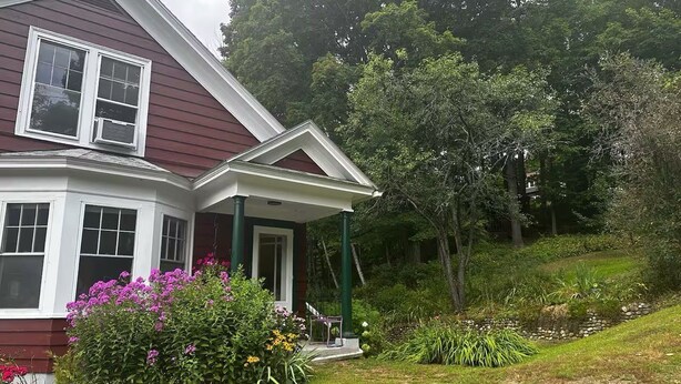 Ein Haus mit Veranda, umgeben von üppigem Grün und blühenden Pflanzen.