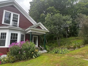 A house with a porch, surrounded by lush greenery and flowering plants.