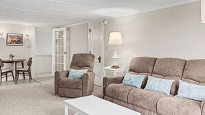 Ein Wohnzimmer mit einer Couch, Sesseln, einem Couchtisch, einer Lampe und einem Essbereich mit Stühlen und Tisch.
