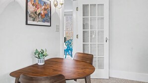 Ein Essbereich mit Holztisch, Stühlen, einer Kühlpflanze, einem gerahmten Gemälde und einer weißen Tür mit satinierten Glasscheiben.