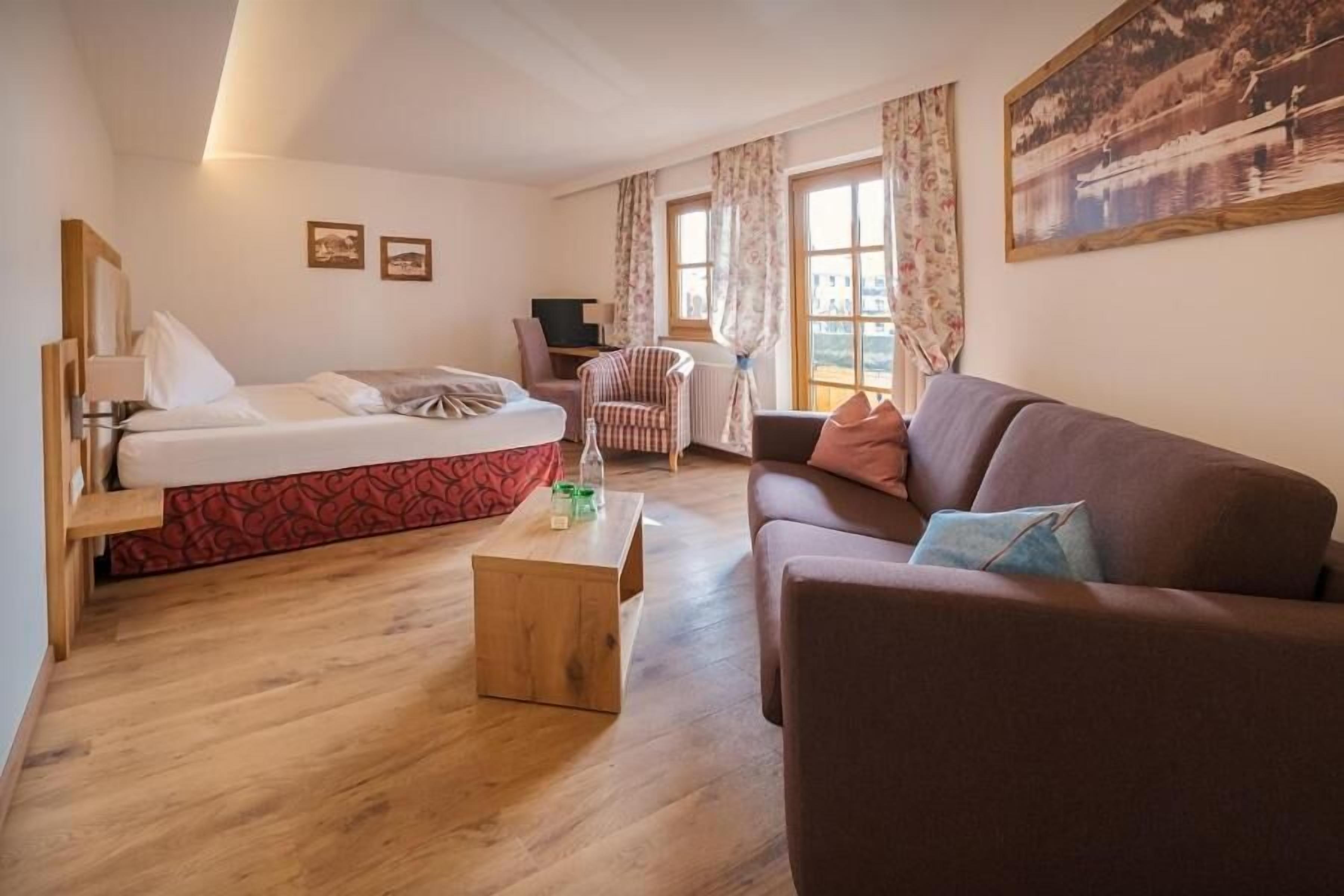 A room with a bed, a sofa, a small table, a chair, and a painting on the wall.