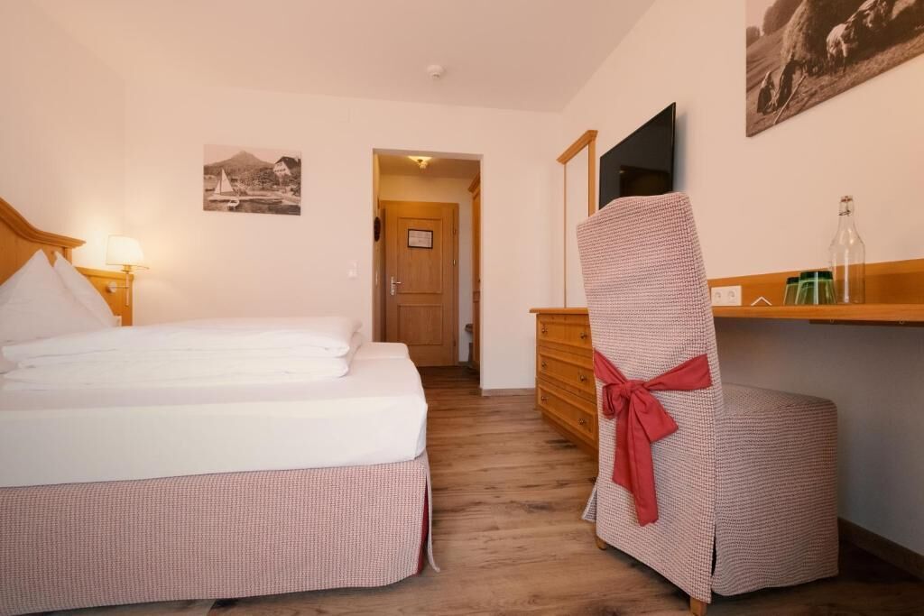 A bedroom with a bed, a chair, a dresser, a mirror, and a door leading to another room.