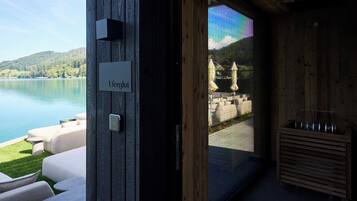 Un edificio moderno con fachada de madera, un cartel que dice 'Uferglut' y vistas a un lago y montañas a través de un vidrio.