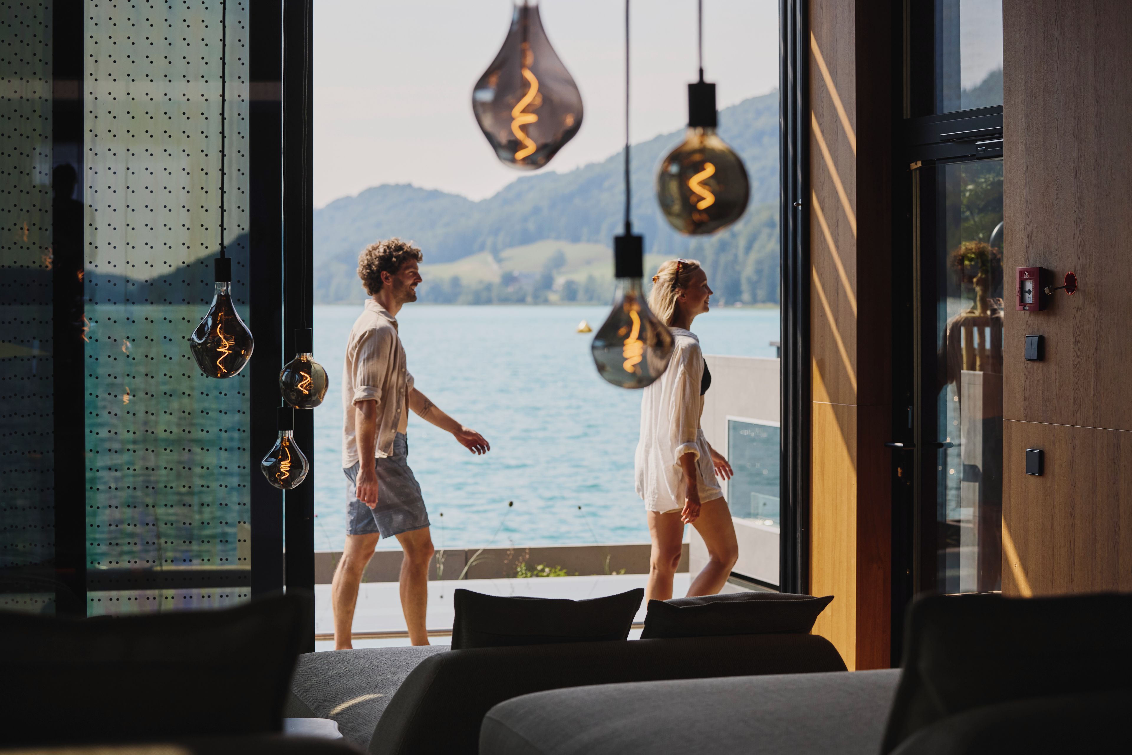A modern interior with a large window overlooking a body of water and mountains.