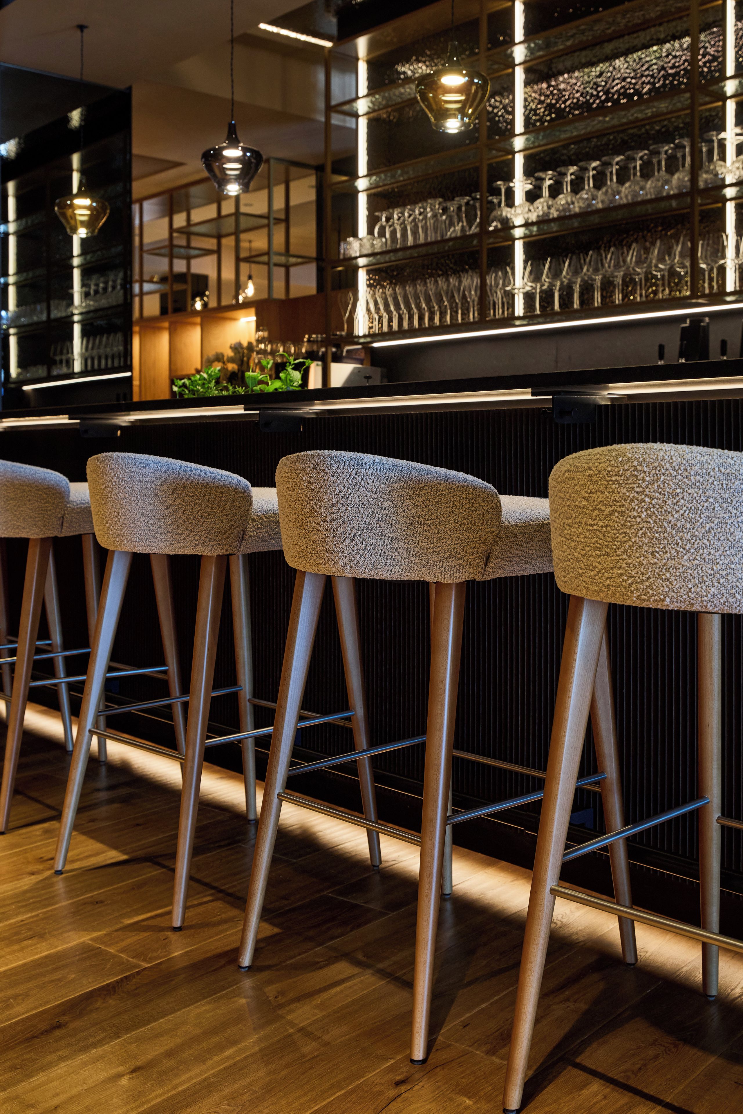 Un espace bar avec des tabourets en bois et une vitrine où sont exposés des verres.