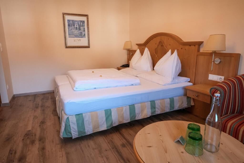 Een hotelkamer met een bed, nachtlampjes, een klein tafeltje met een fles en een lijstje aan de muur.