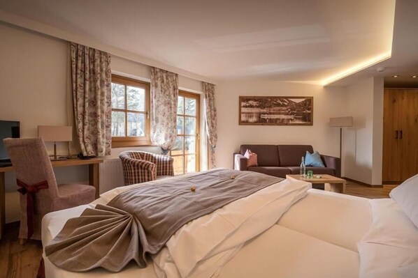 A hotel room with a bed, a desk, a chair, a sofa, and a painting on the wall. - Vogl's Nest (Fuschl am See)