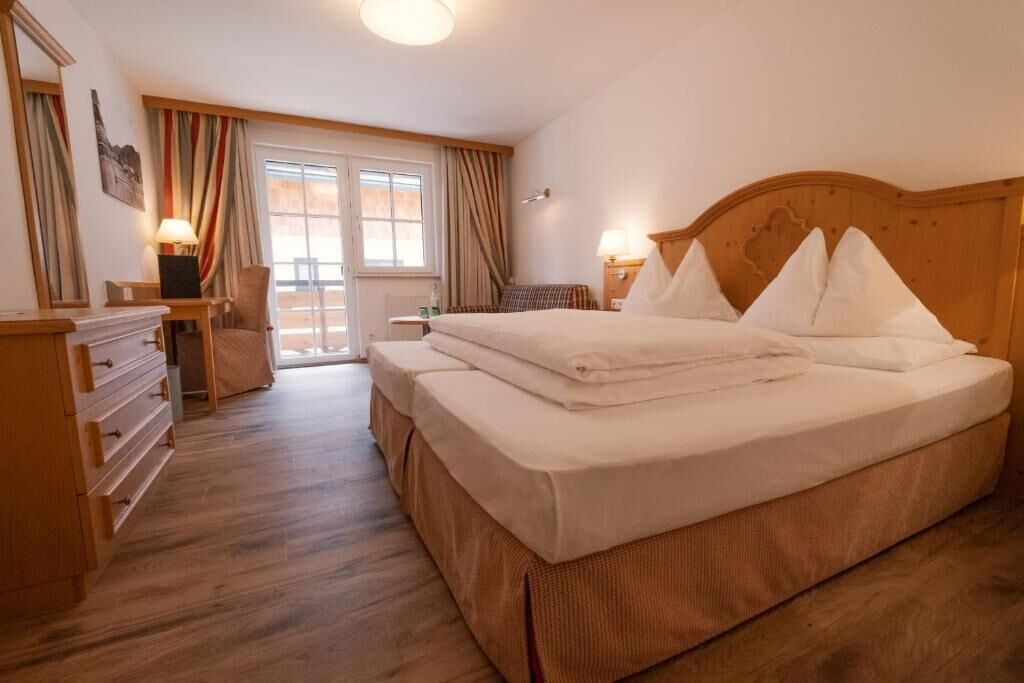 Une chambre d’hôtel avec un lit, un bureau, une chaise, une commode et une fenêtre avec des rideaux.
