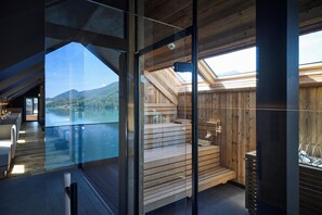 A modern interior with a glass wall offering a view of a lake and mountains. - Vogl's Nest (Fuschl am See)