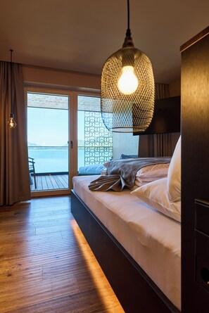A bedroom with a bed, a hanging light fixture, a view through a glass door, and a wooden floor. - Vogl's Nest (Fuschl am See)