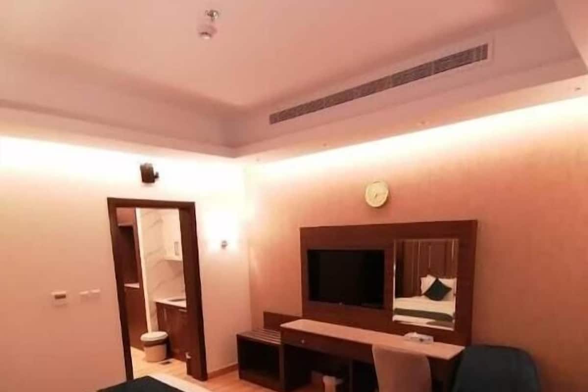 Une chambre d’hôtel avec deux lits, un bureau, une chaise, une télévision et une horloge au mur.