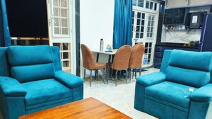 A living room with two blue armchairs, a wooden coffee table, and a dining table with chairs.