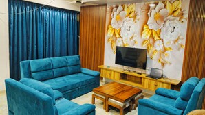 A living room with a blue sofa set, a wooden coffee table, a flat-screen TV, and a decorative wall with floral patterns.