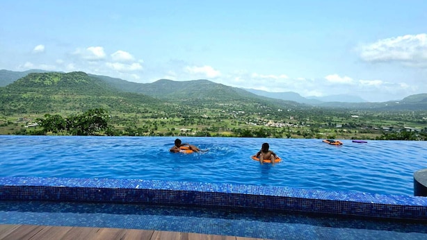 A swimming pool with two people, surrounded by a mountainous landscape.