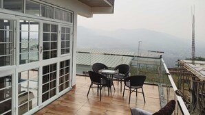 A balcony with a table and chairs, a view of the mountains, and a building with large windows.