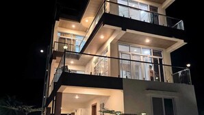 A multi-story building with balconies, large windows, and a well-lit facade at night.