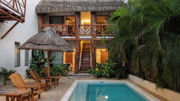 A pool area with lounge chairs, a thatched umbrella, and a staircase leading to an upper level. - 9BR Villa | Sleeps 24 | Private Pool + Rooftop | Concierge & Breakfast Included (Tulum)