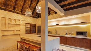 A modern kitchen with wooden bar stools, a thatched ceiling, and a basket of towels. - 9BR Villa | Sleeps 24 | Private Pool + Rooftop | Concierge & Breakfast Included (Tulum)