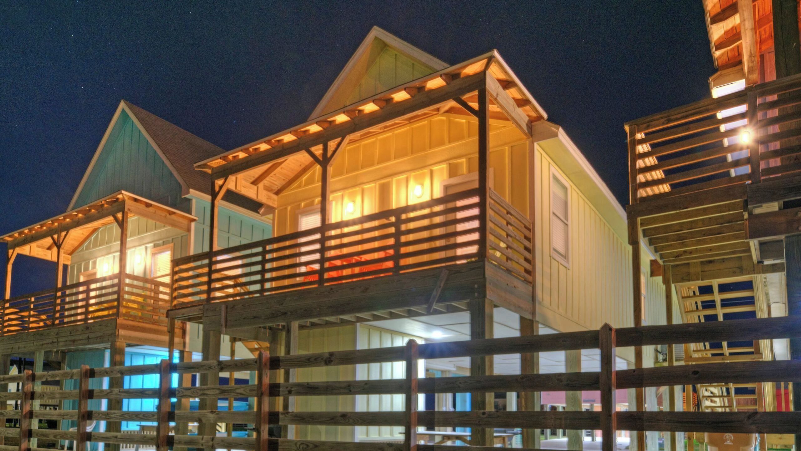 A waterfront property with multiple buildings, a wooden deck, and a covered area with lights.