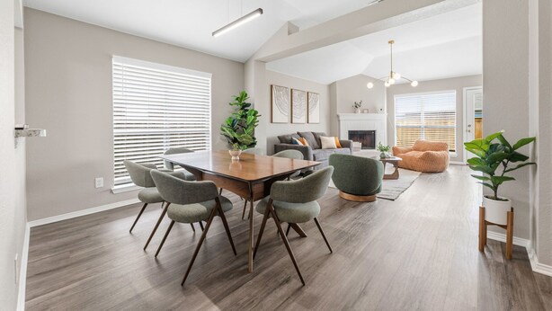 A modern living room with a dining table, chairs, a sofa, a fireplace, and a staircase leading to another level. - Lake Haven Retreat - Spacious 3BR Family Escape Near Lake Lewisville (Little Elm)